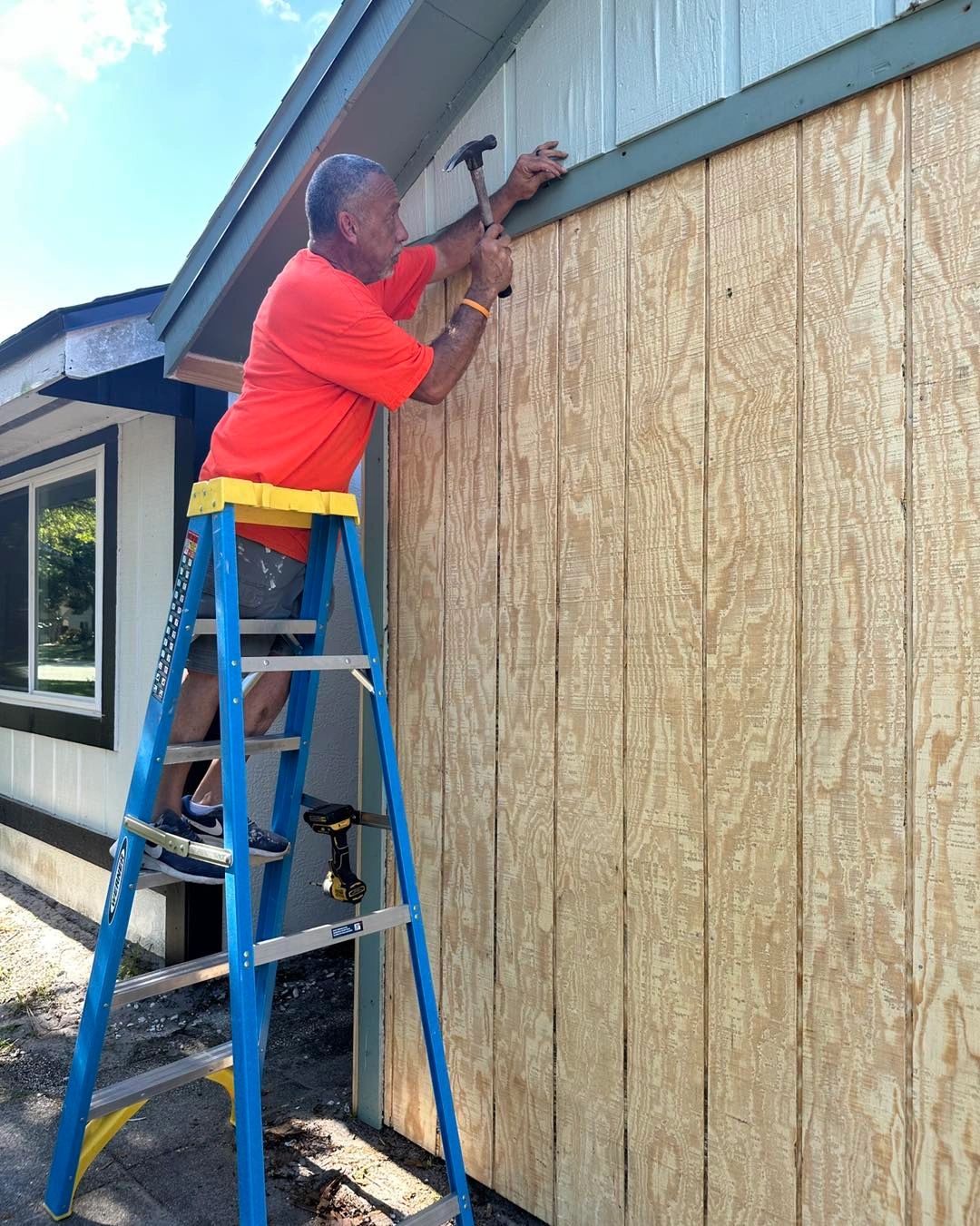 Julio on a tall ladder installing vertical siding