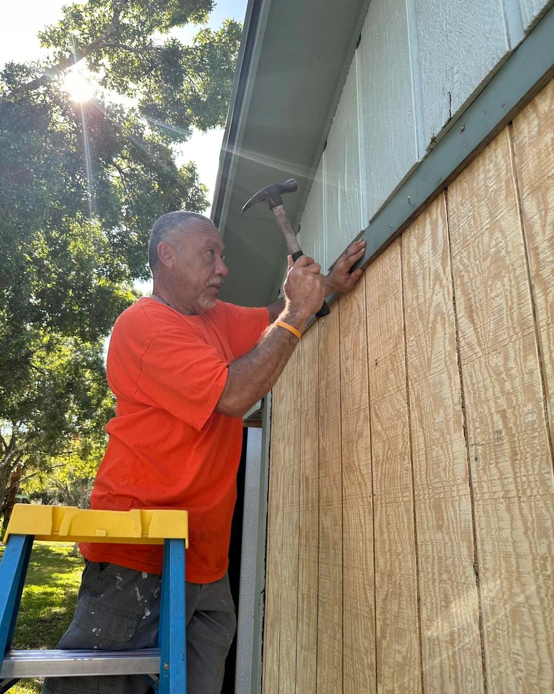 Julio on a ladder installing siding, orange work shirt