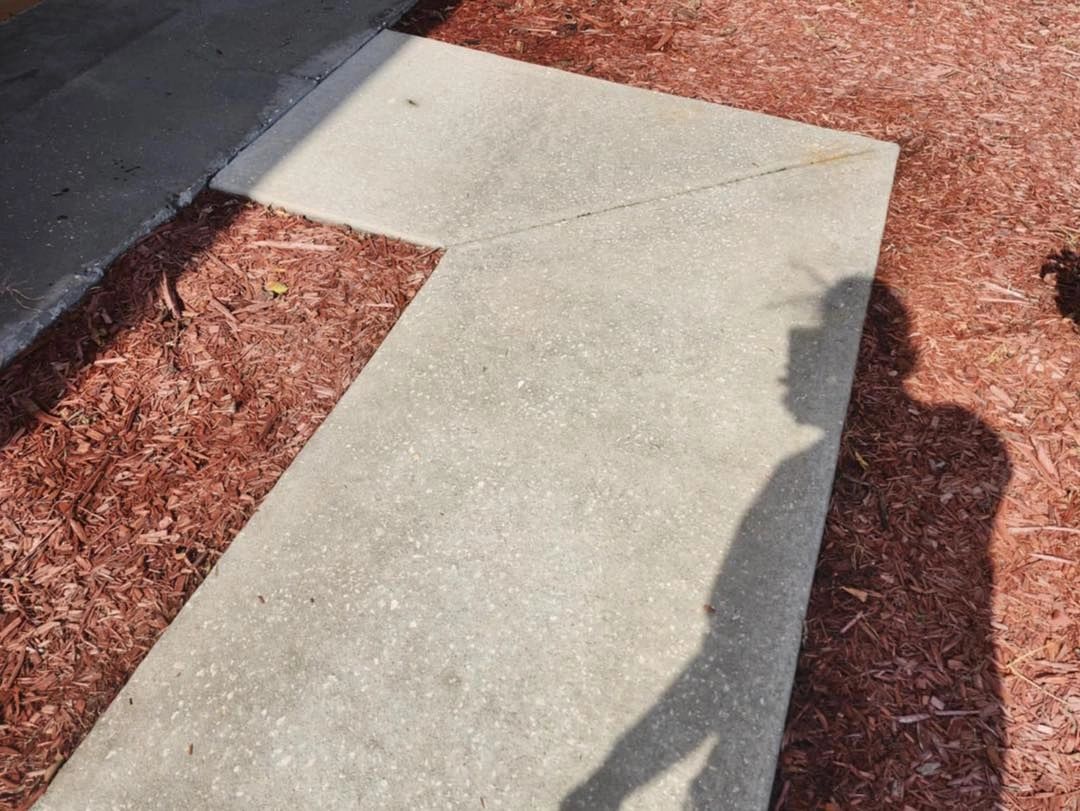 Clean L-shaped concrete walkway beside red mulch
